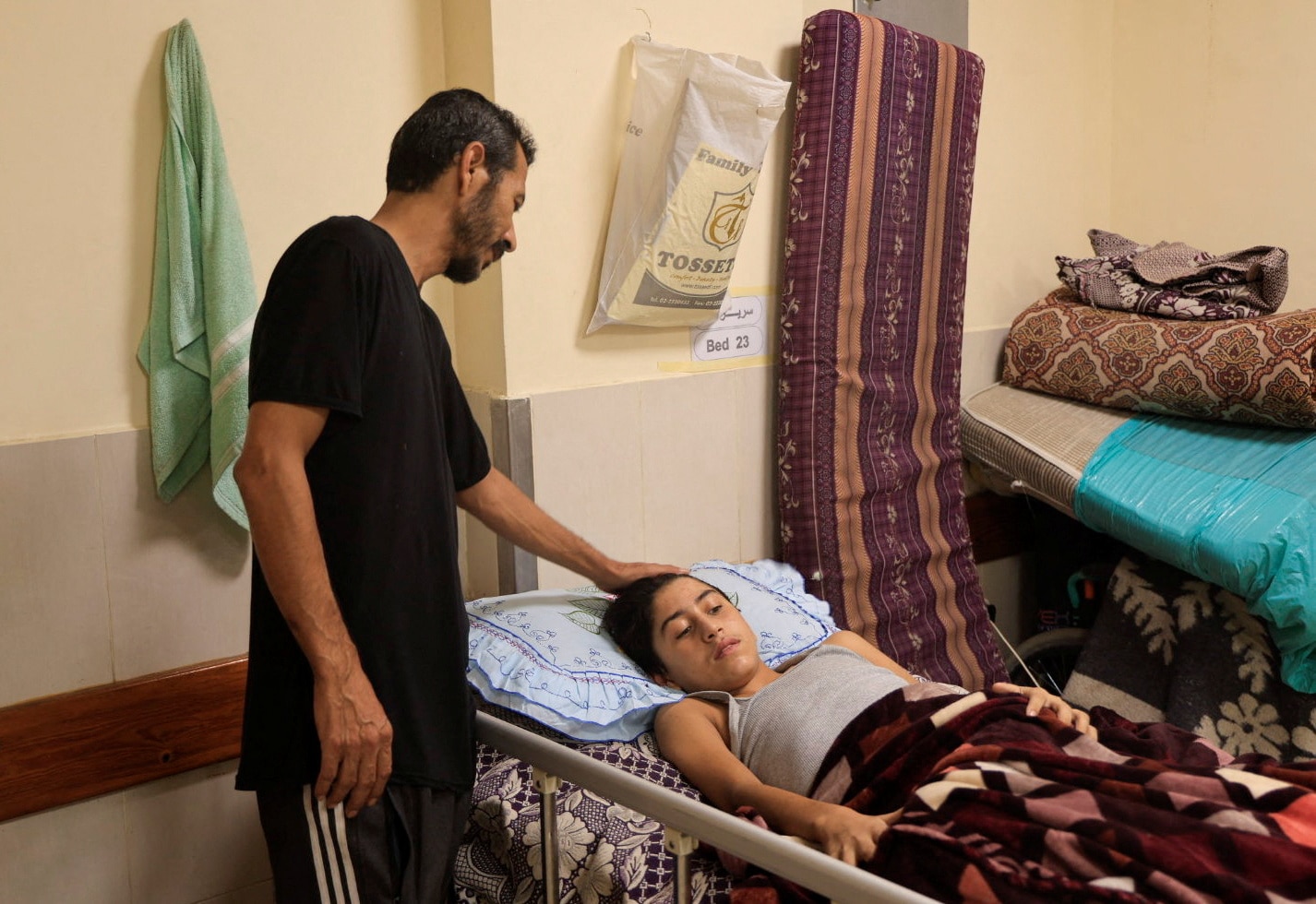 A man stands next to a young boy in a hospital bed in Gaza. 