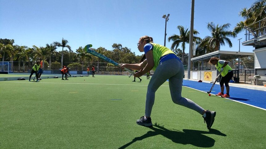 A female hockey player hit a ball with a hockey stick on a green field.