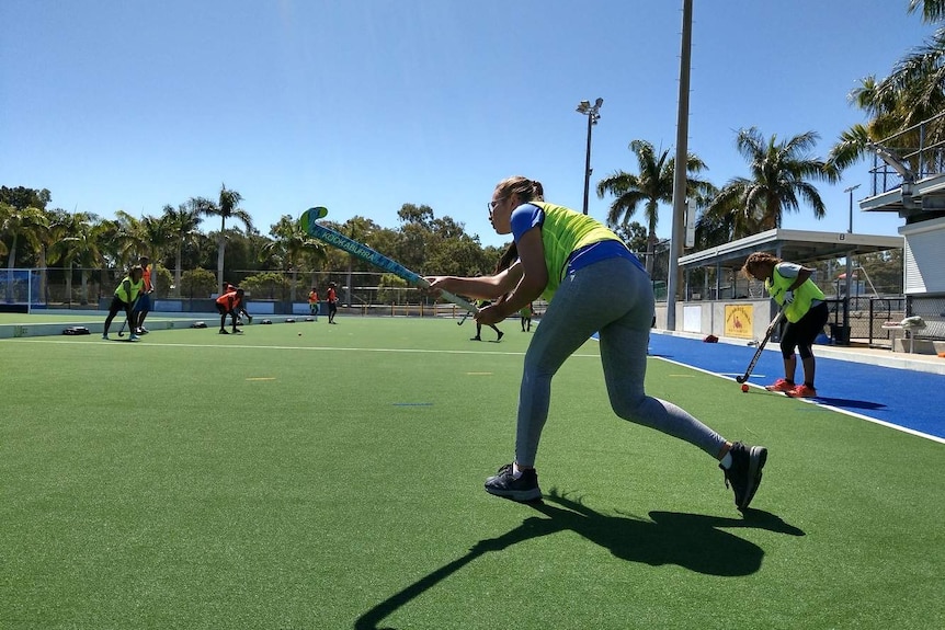 A female hockey player hit a ball with a hockey stick on a green field.