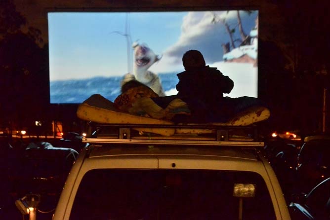 Silhouette of a child sitting on a car roof, watching a children's move at the Drive-In Cinema.