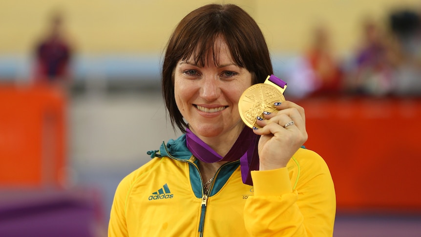 Anna Meares stands holding her 2012 Olympic gold medal with her left hand.