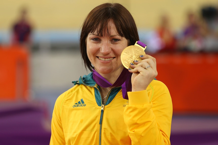 Anna Meares stands holding her 2012 Olympic gold medal with her left hand.