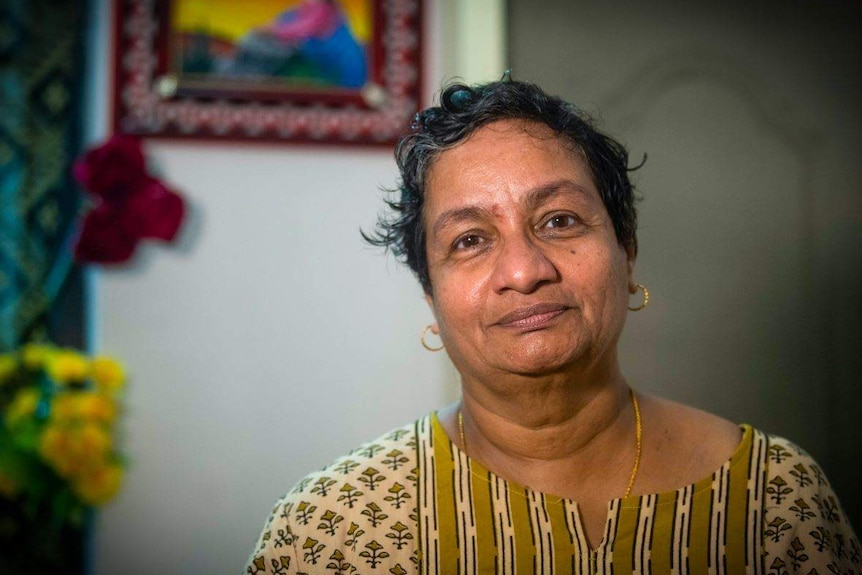 Sister Jesme looks at the camera, there is a religious picture on the wall behind her.