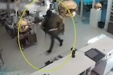 A CCTV still of a man in a black hood and holding a painting while running through a gift shop.