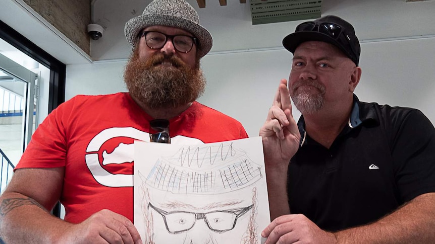 Auslan art tour participant Michael Lockrey stands next to his friend Denis Mulane who holds the 'portrait' by Michael