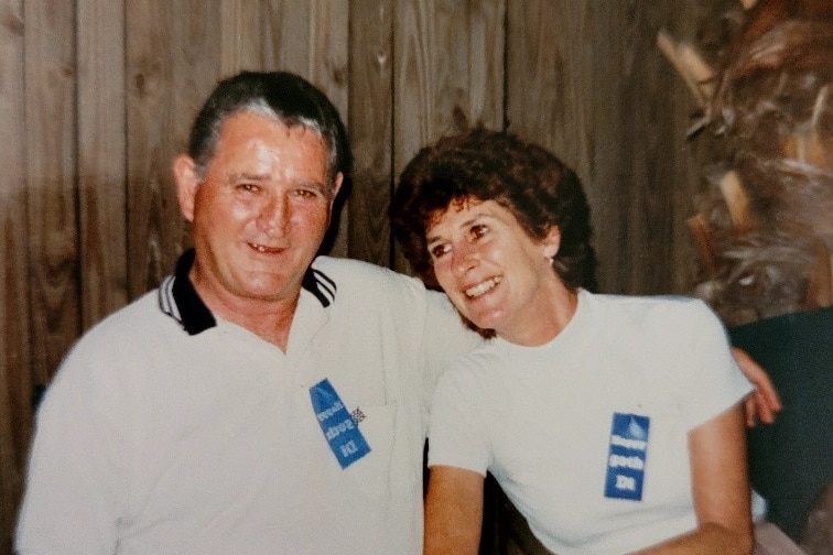 An old looking photo of a man and woman sit together smiling, they are wearing white shirts