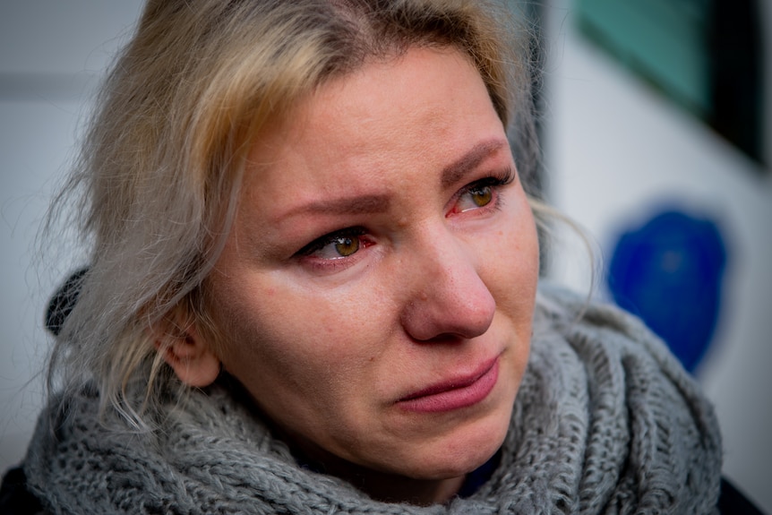 A close up of a woman with blonde hair and tears in her eyes.