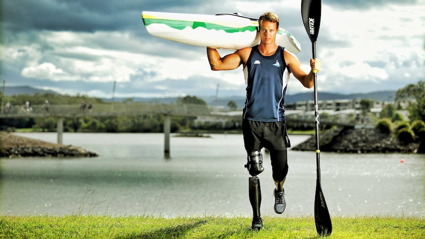 Man with prosthetic limb holds a kayak on his shoulder.