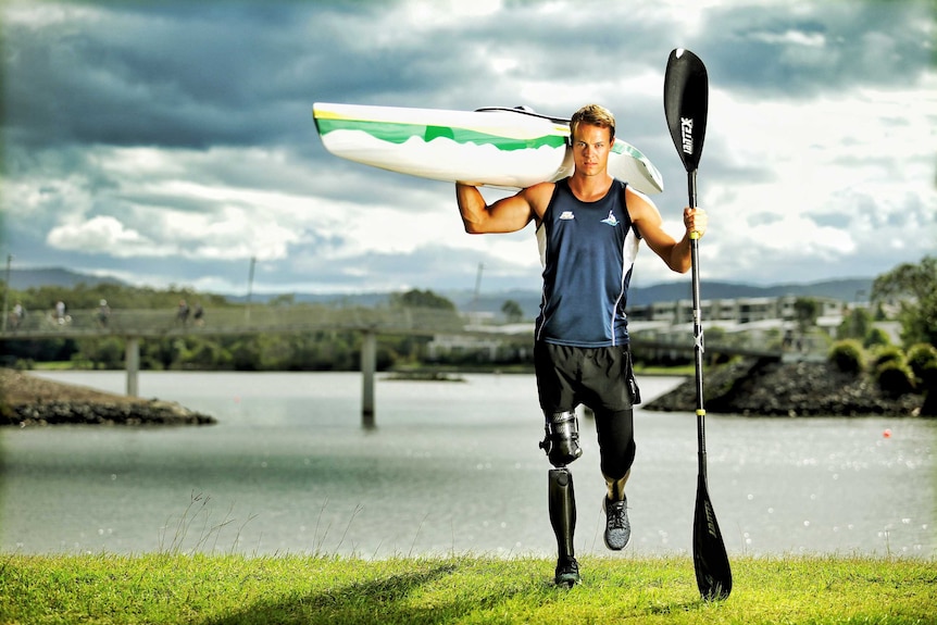 Man with prosthetic limb holds a kayak on his shoulder.