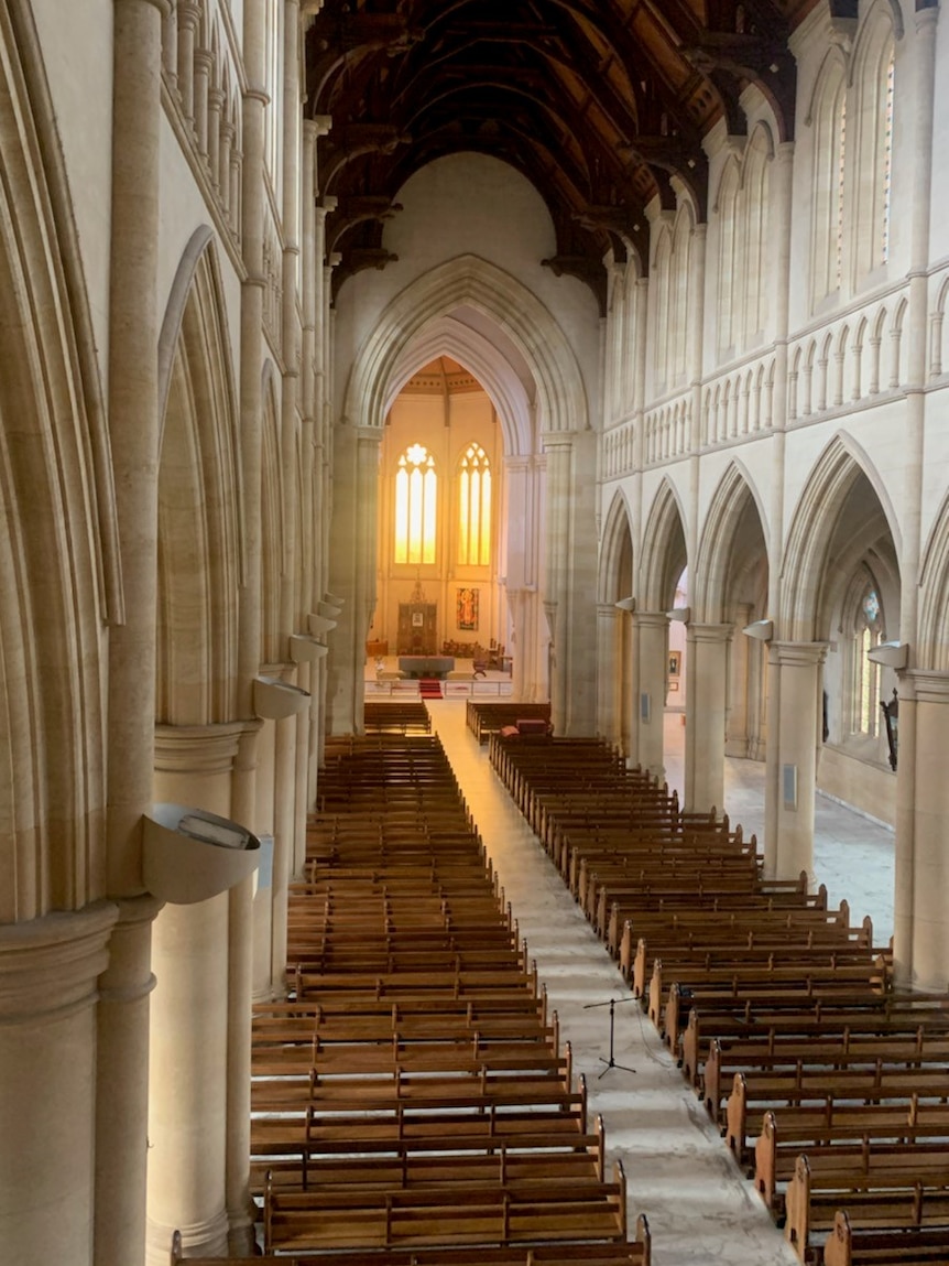 Inside a large gothic cathedral, its ceiling is several stories high. Dozens of pews fill the space.