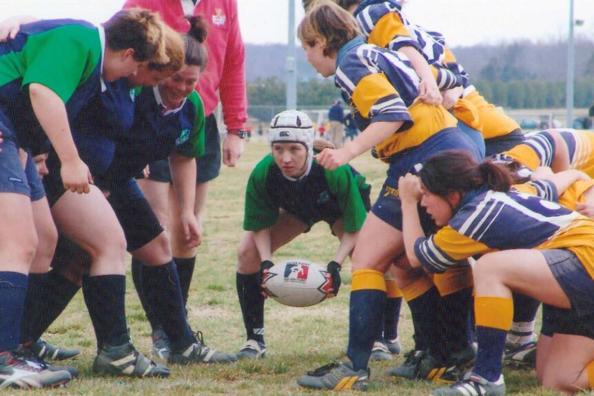 Sara Edwards Rohner, wearing protective headgear, holds the ball during a rugby match.