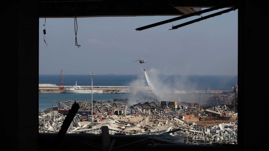A Lebanese army helicopter seen through a damaged apartment drops water  on debris.
