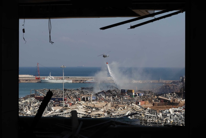 A Lebanese army helicopter seen through a damaged apartment drops water  on debris.