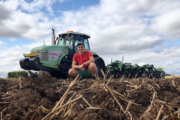 girl squats in a paddock in front of a tractor