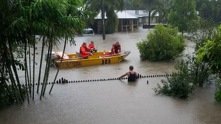 Men on a boat on a flooded street stops to speak to a man who is chest deep in water.