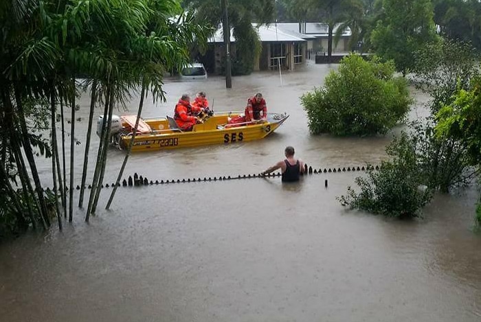 Men on a boat on a flooded street stops to speak to a man who is chest deep in water.