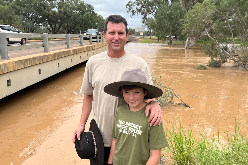 A man and his son stand in front of a swollen creek. 