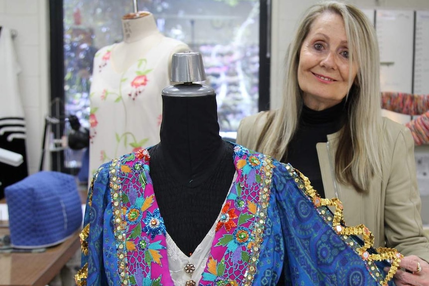 Woman with blond hair holds sleeve of very colourful dress