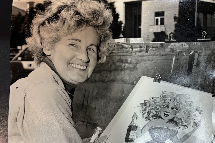 black and white photo of woman smiling at camera as she draws a cartoon