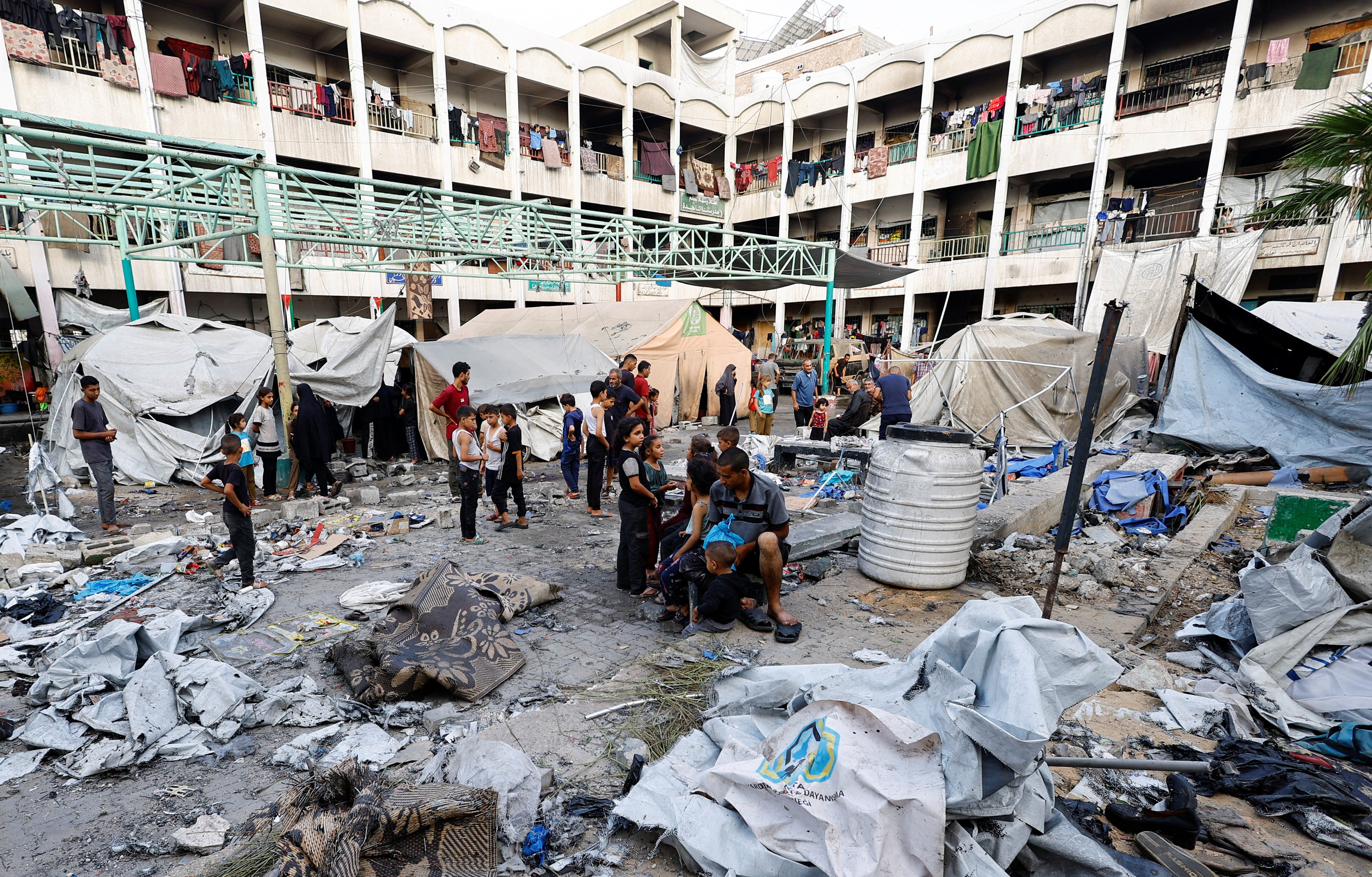 A building with many people standing around rubble and rubbish with some make shift tents