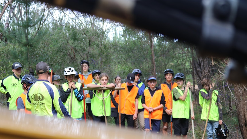 I group of young people, some leaning on garden tools and wearing bike helmets.