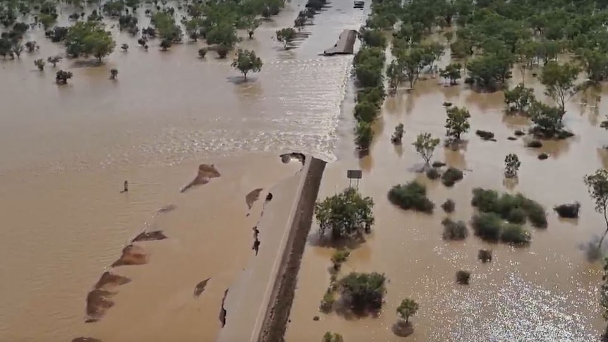 Floodwaters across a highway with extensive damage to the road. 