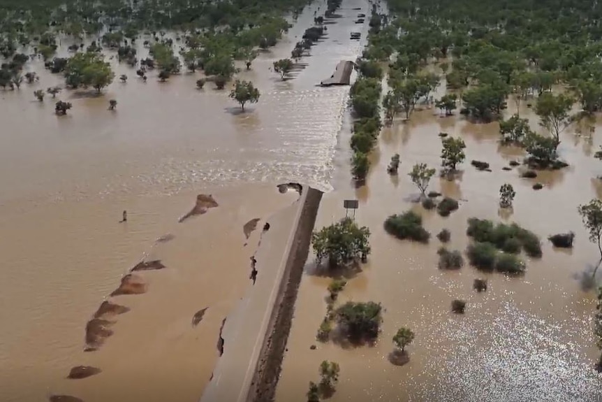 Floodwaters across a highway with extensive damage to the road. 