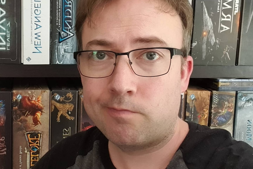 Adam Brown, a man wearing glasses, smirks for a selfie.