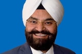 Gurpal Singh smiles for a portrait photograph, in front of a blue background.