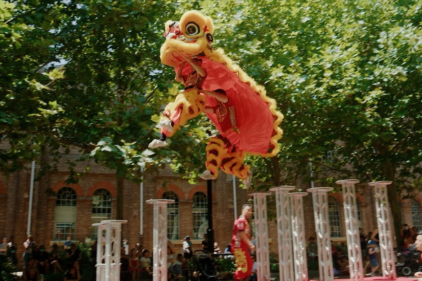 A yellow and red Chinese lion costume jumps between tall poles