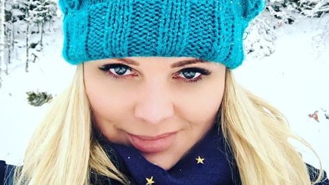 A photo of a young blonde-haired woman wearing a blue beanie in a snowy location.