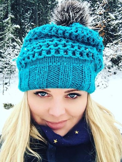 A photo of a young blonde-haired woman wearing a blue beanie in a snowy location.