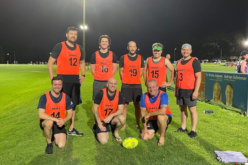 A men's touch football team, standing together on a field under lights at night.
