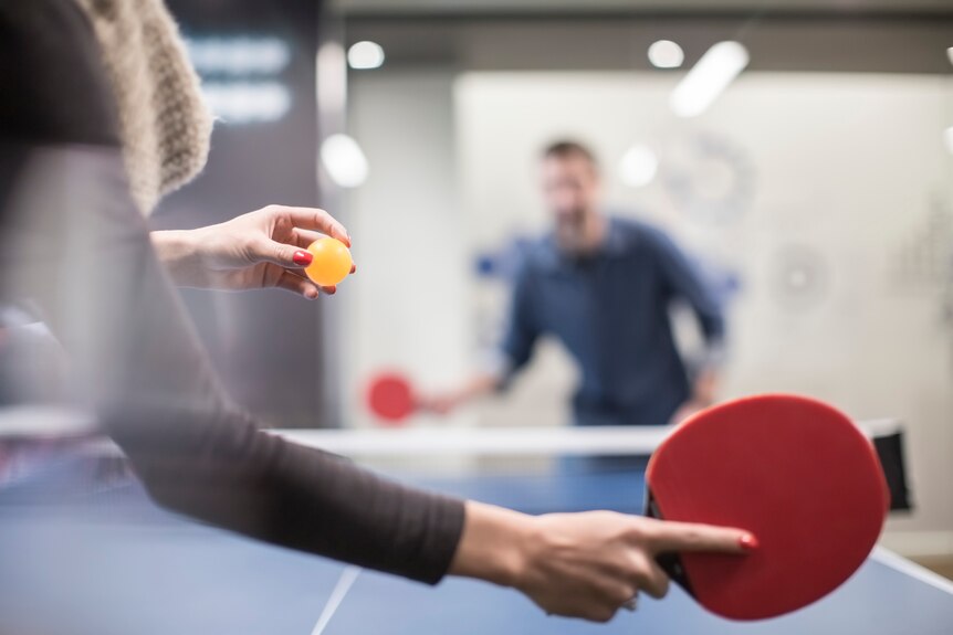 A male and a female work colleague face off in a game of ping pong