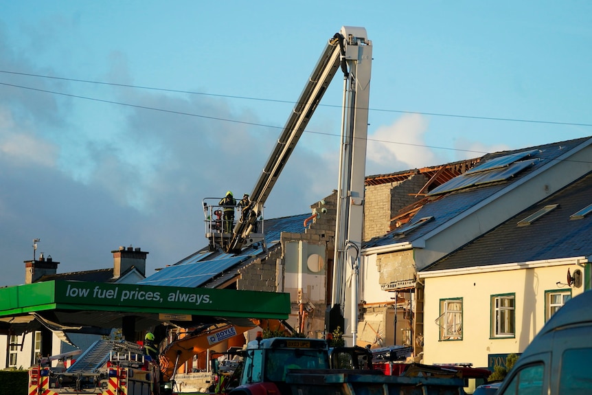 A person on a cherry picker is lifted above the destroyed roof of a petrol station. 