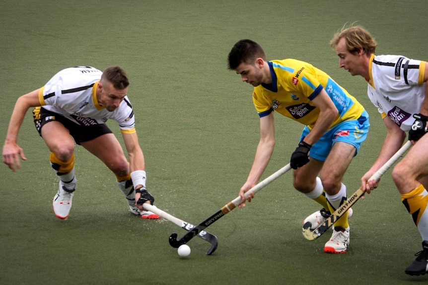 An action shot of Davis Atkin (middle) playing hockey with two other men.