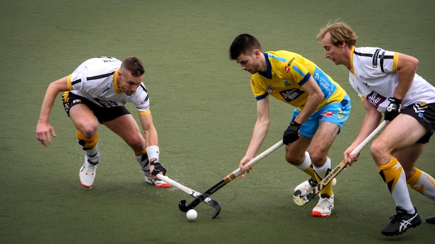 An action shot of Davis Atkin (middle) playing hockey with two other men.