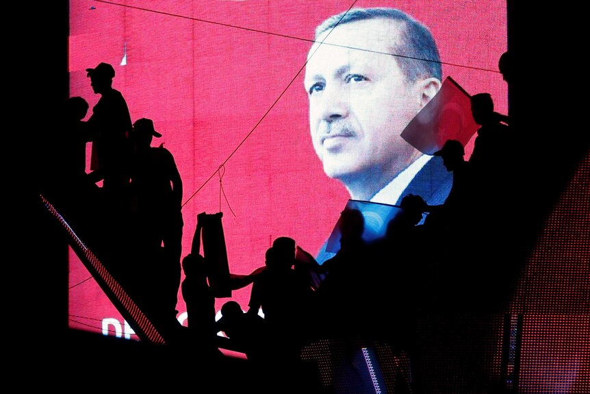 Turkish Supporters are silhouetted against a screan showing President Tayyip Erdogan