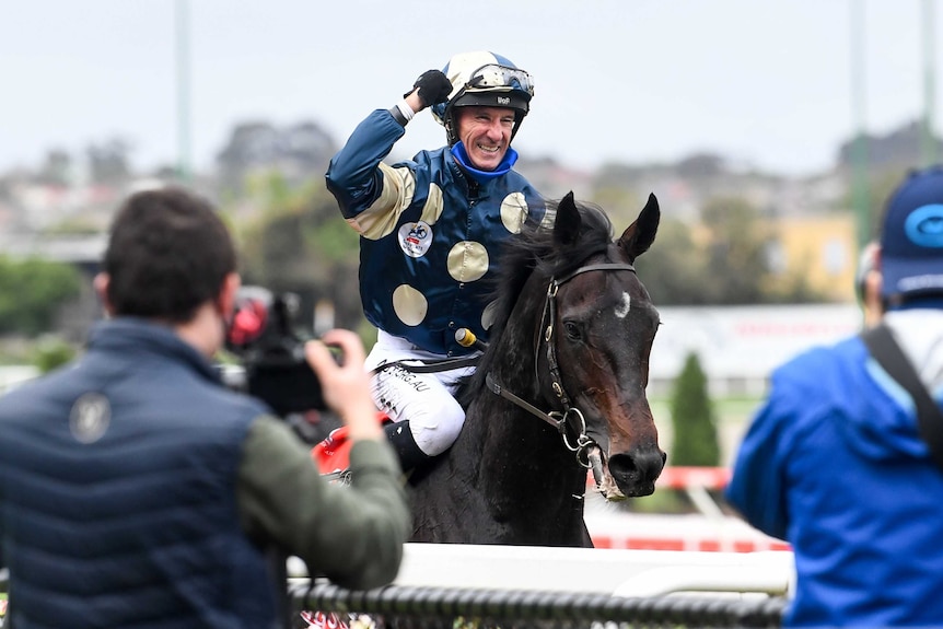 A jockey smiles and pumps his right fist while riding atop the horse that won the Cox Plate.