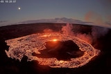 Lava flows in a circle inside a volcano with the sky seen in background. 