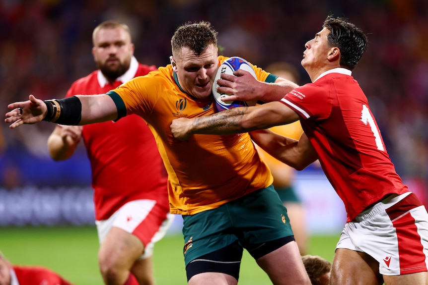 A Wallabies player holds the ball as he is tackled by a Welsh opponent.