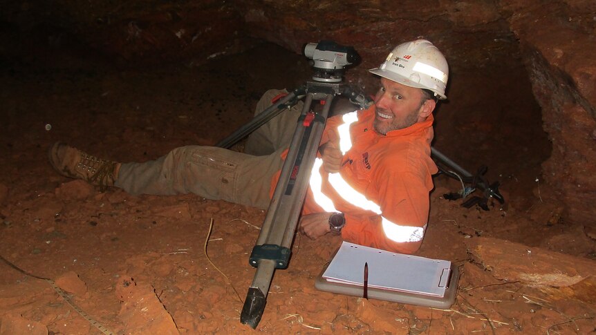 a man lying down in a cave next to a laser level kit