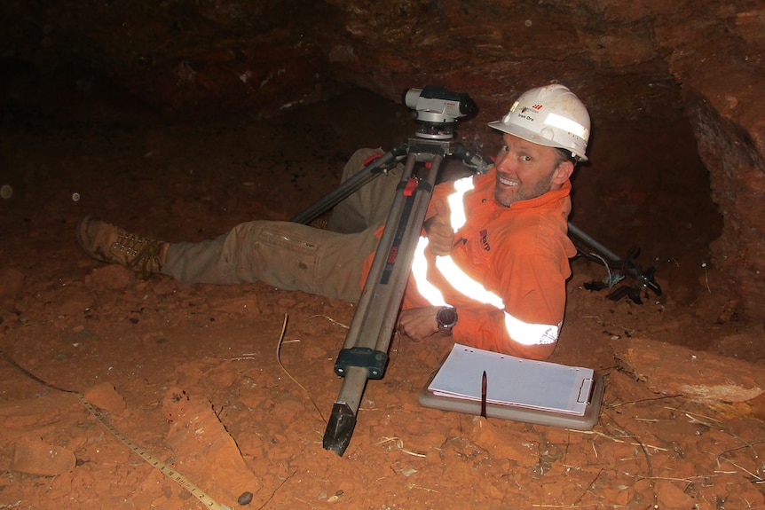 a man lying down in a cave next to a laser level kit