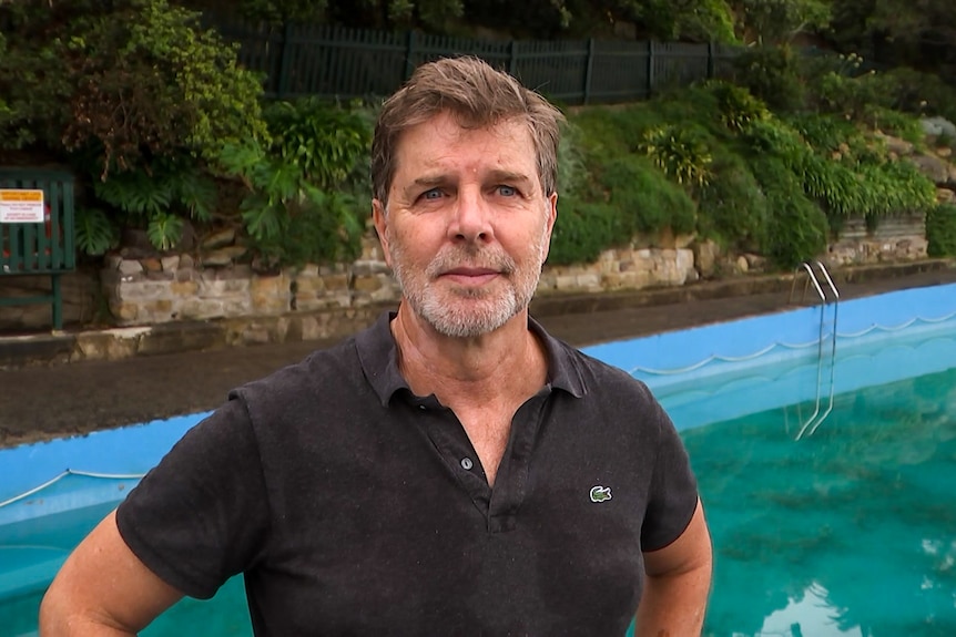 A man, wearing a black shirt, stands in front of a saltwater public pool.
