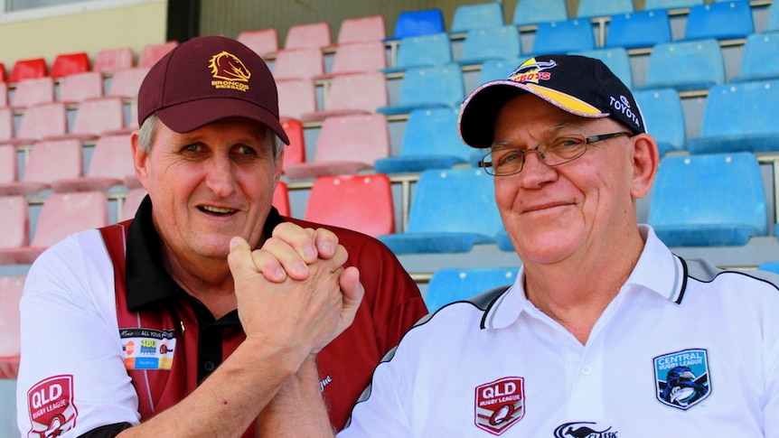 BRL chairman Mike Ireland, wearing a Broncos cap, arm wrestles Dave Pearce from QRL wearing a Cowboys cap.