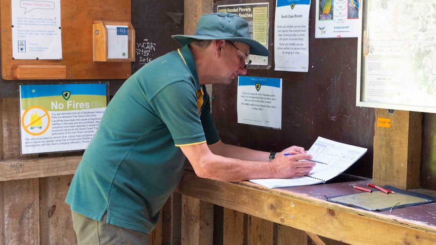 A man in a green uniform checks a log book