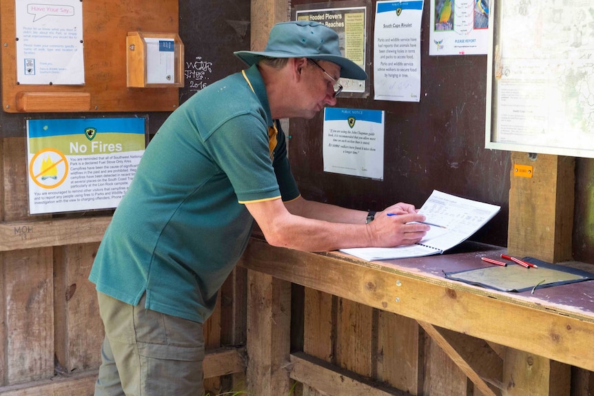 A man in a green uniform checks a log book