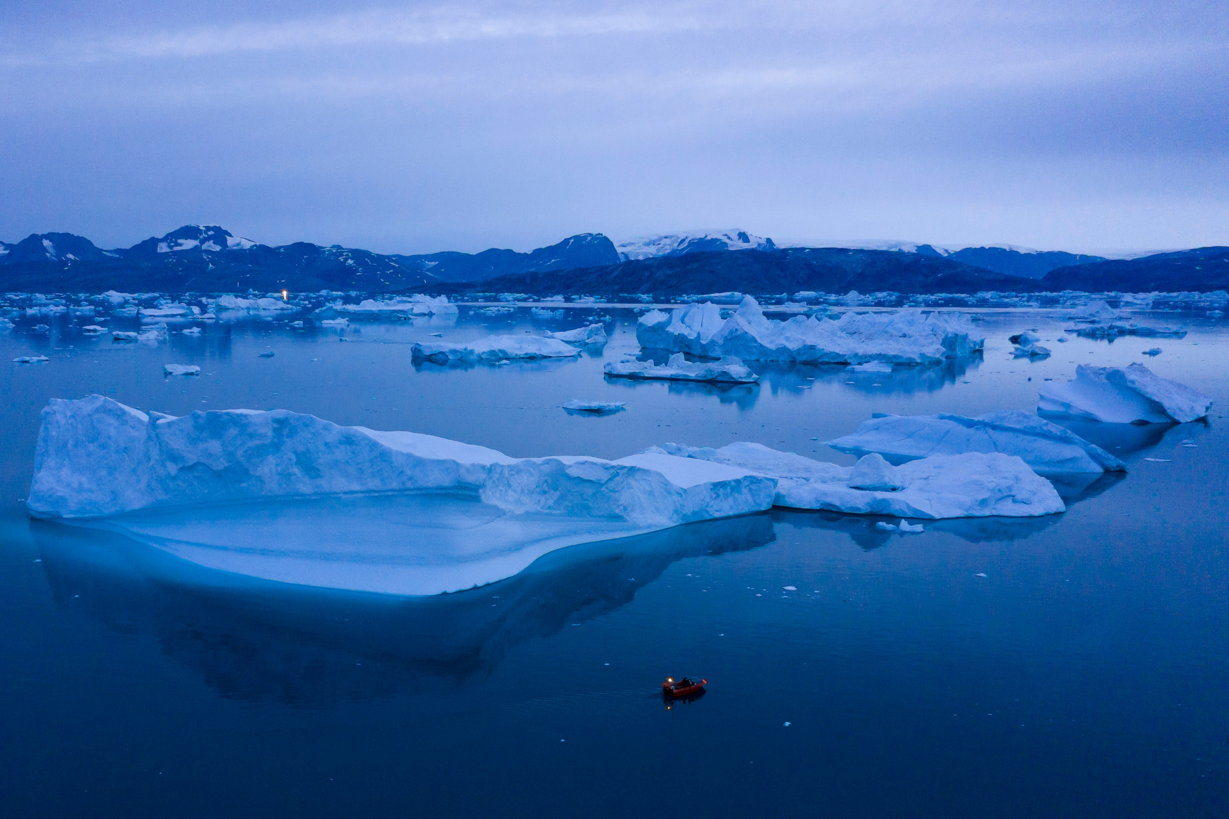 Floating icebergs dot a deep blue sea in low, blue light of the Arctic.