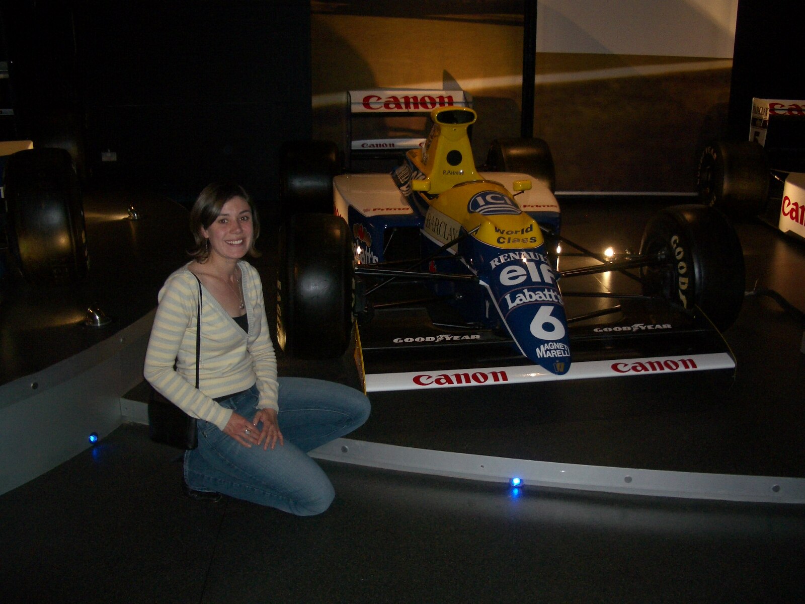 A young woman in the mid 2000s crouched next to a race car