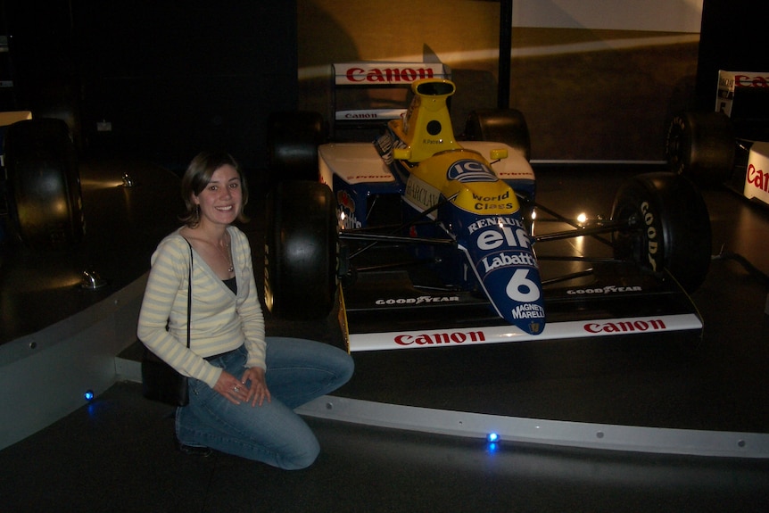 A young woman in the mid 2000s crouched next to a race car
